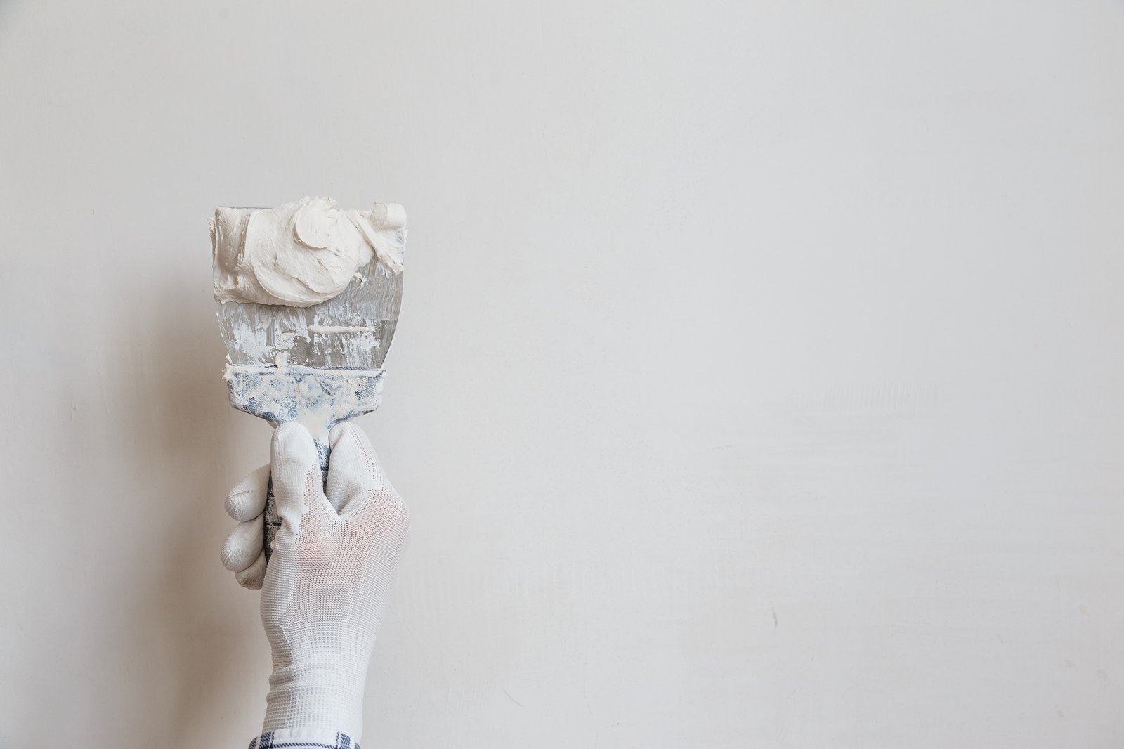 Worker in white gloves performs plastering of the walls of the room